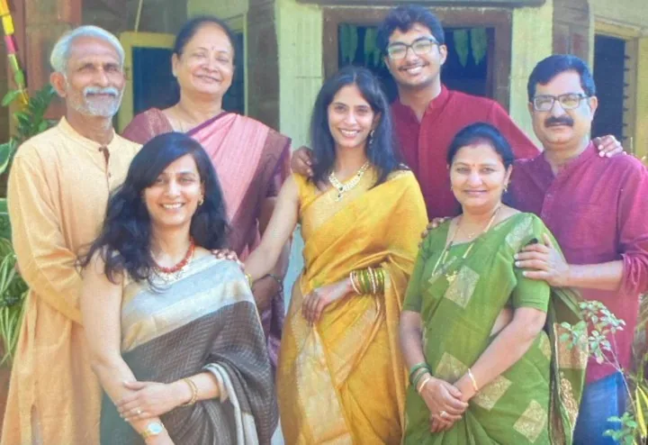 Both families together in front of a house, Anarghya in a yellow saree and Ruthuparna in a maroon kurta